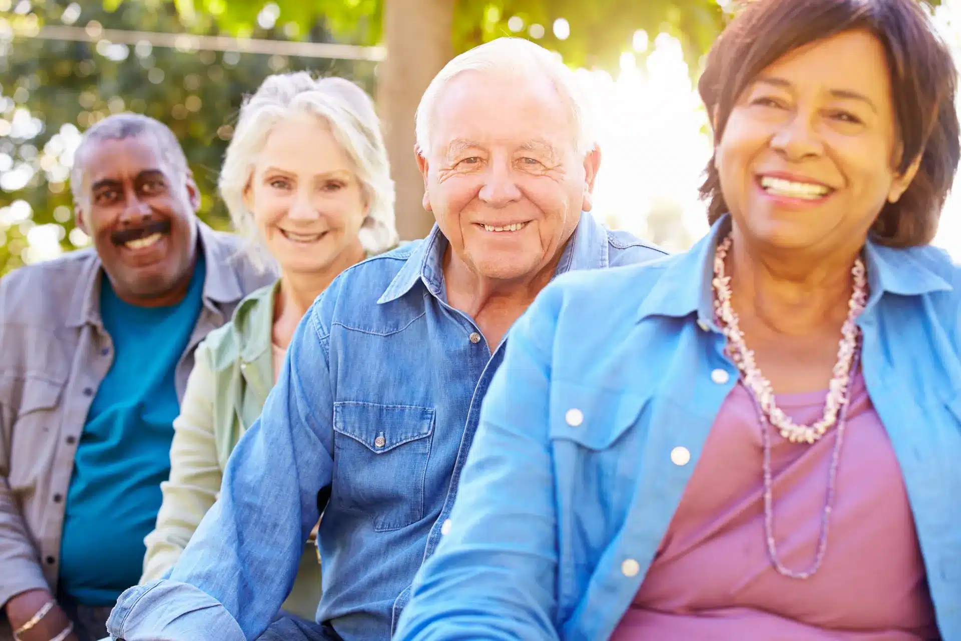 Group of smiling older adults standing together outdoors in a bright community setting.